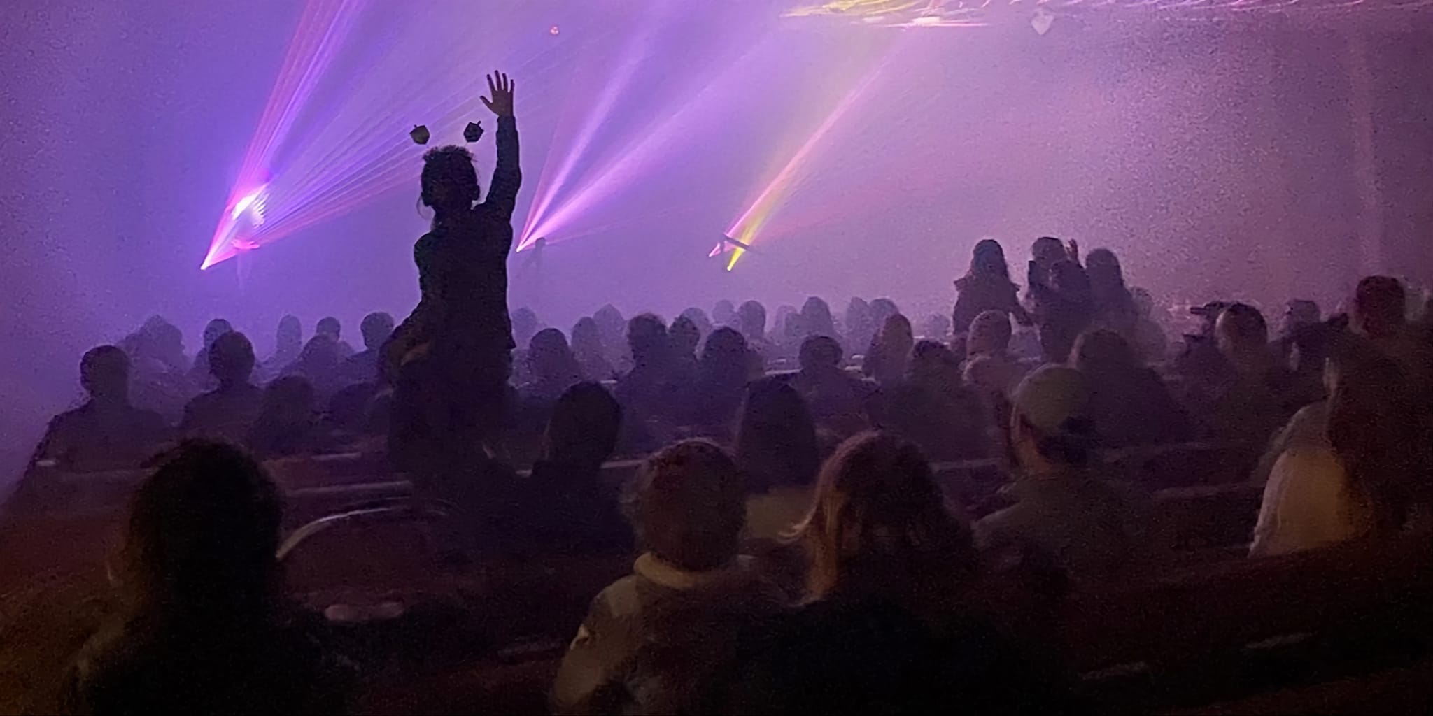 Crowd silhouettes facing the stage under sweeping purple laser beams
