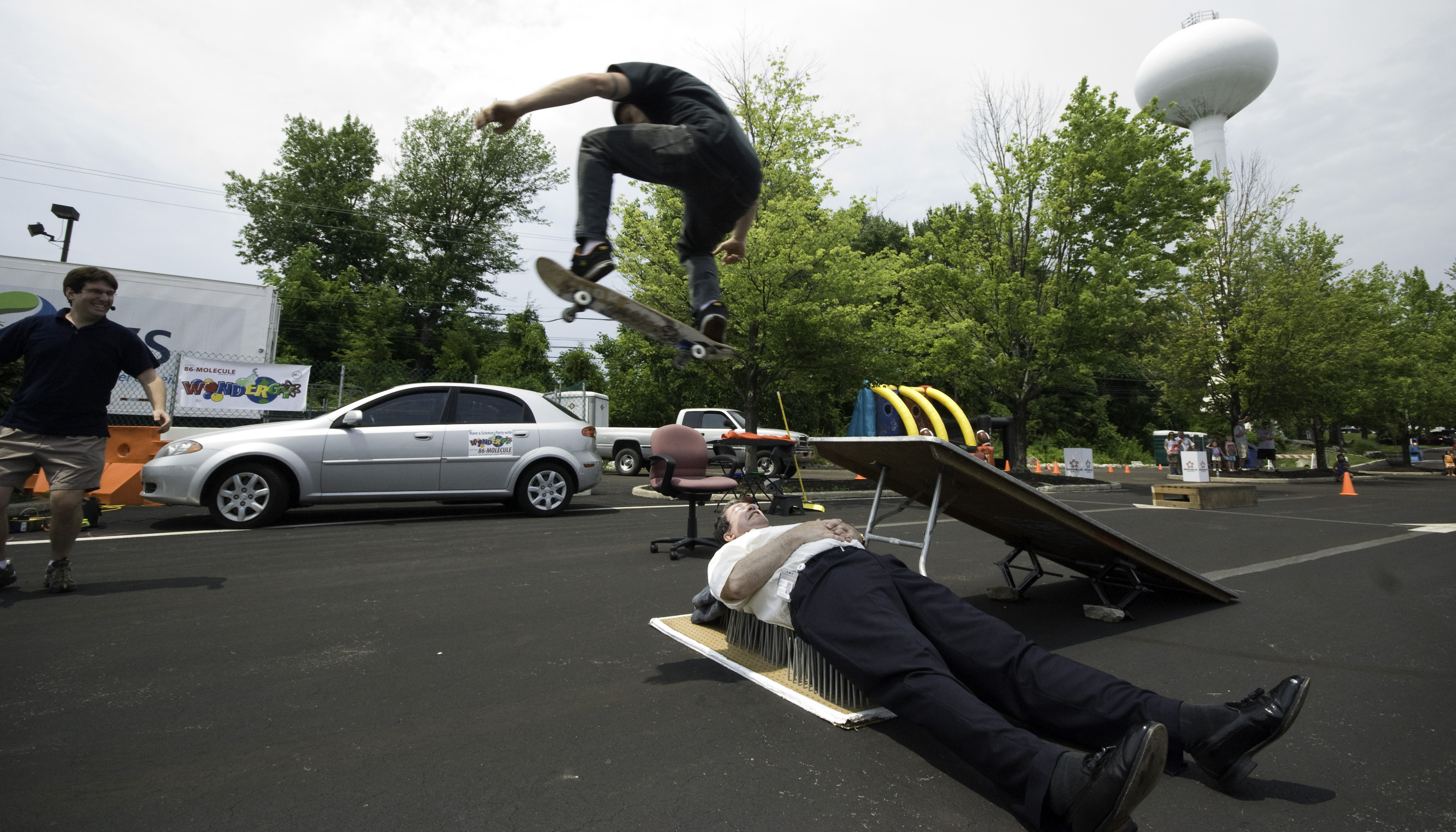 A skateboarder mid-jump soaring over a car during a Skate Science physics demonstration